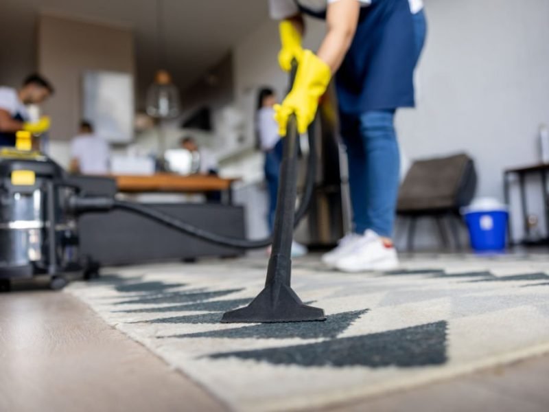 Close-up on a professional cleaner vacuuming a carpet while working at an apartment - housework concepts